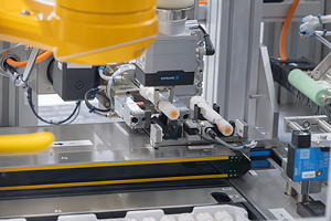 Stabiles automatisiertes Handling selbst bei komplexen Produktgeometrien: Während der Greifer einen etikettieren Autoinjektor zurück ins Tray legt, bewegt die Transport- und Rotationseinheit bereits ein neues Produkt Richtung Spendekante des Etikettierers.